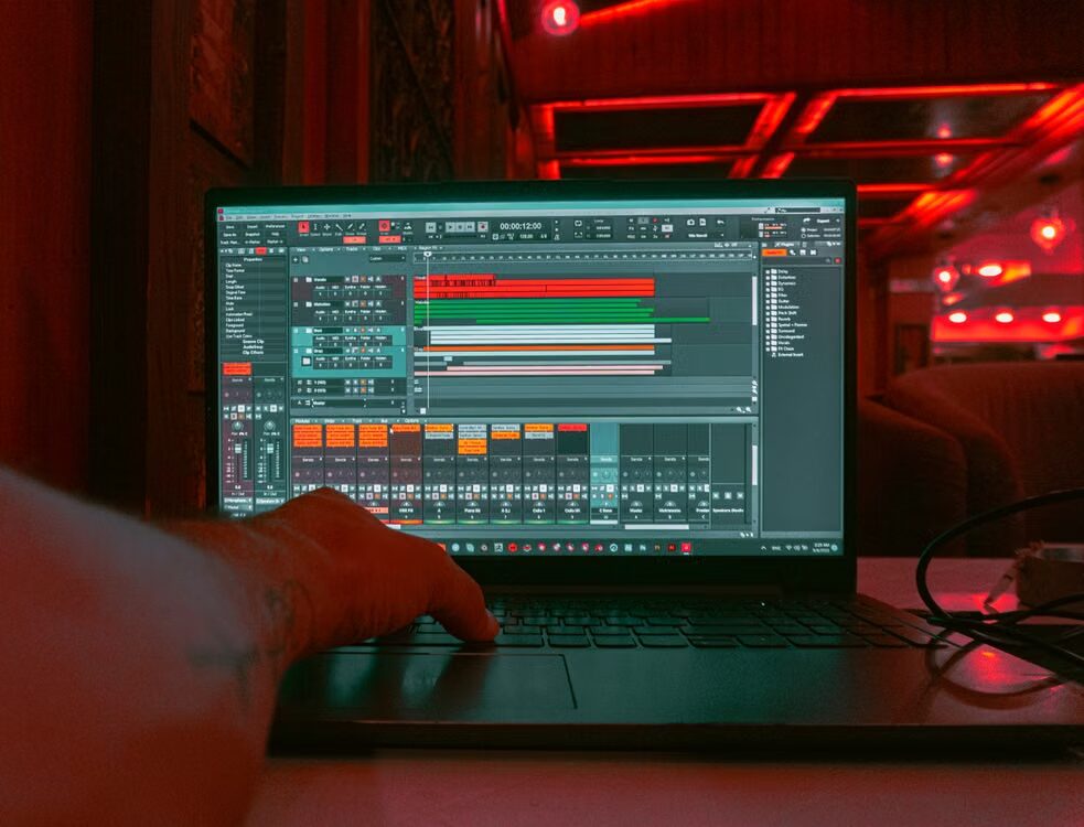Person using audio editing software on a laptop in a red-lit recording studio.