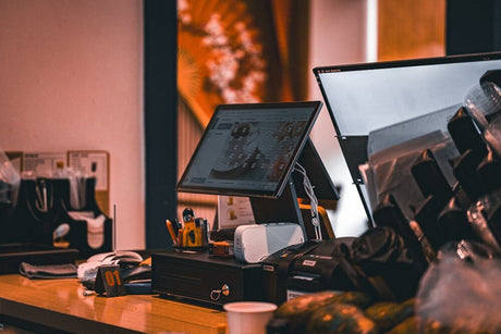 Small business checkout counter with POS screens, receipt printer, and office equipment.